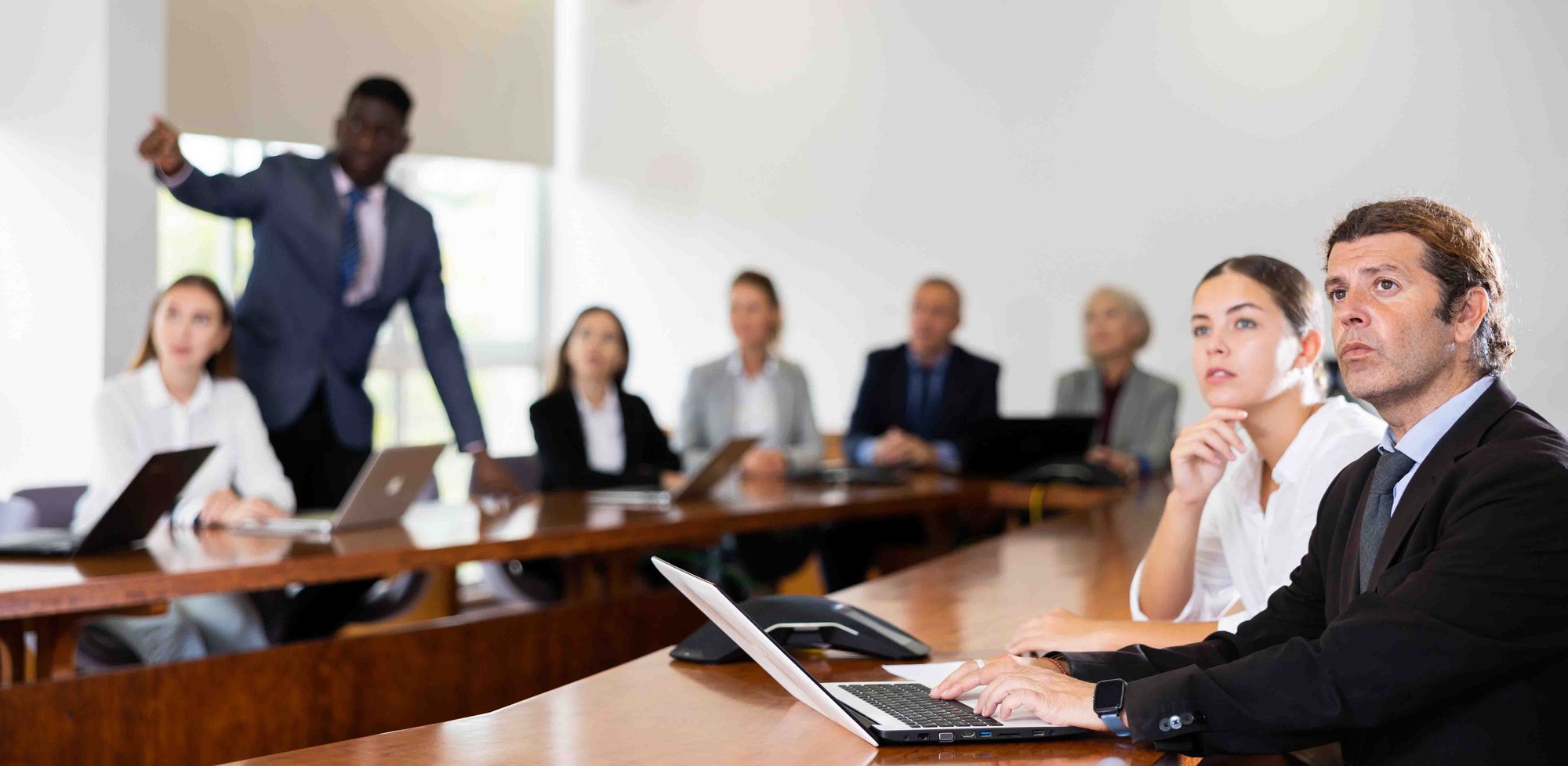 Side portrait of mid aged white dark-haired male manager attending business meeting in conference room and interestedly watching colleagues presentation