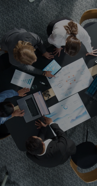 Overhead view of business professionals collaborating around a conference table with laptops, tablets, and data reports
